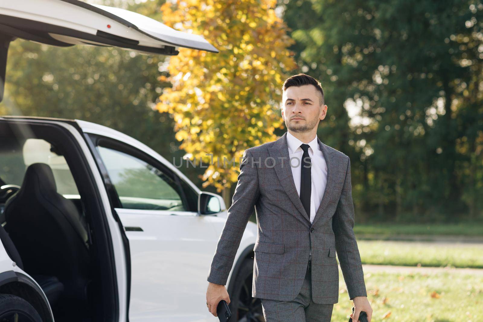 The man gets out of the car. Man in a strict business suit opens the door and gets out of a luxury car.