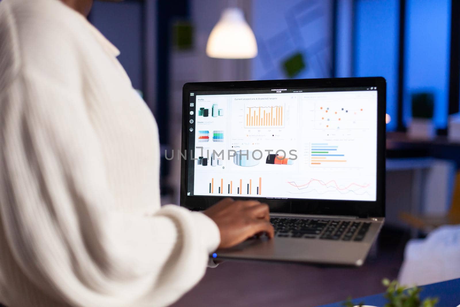 Close up of african woman working overtime late at night in office using laptop. Busy focused employee using modern technology network wireless overtime.