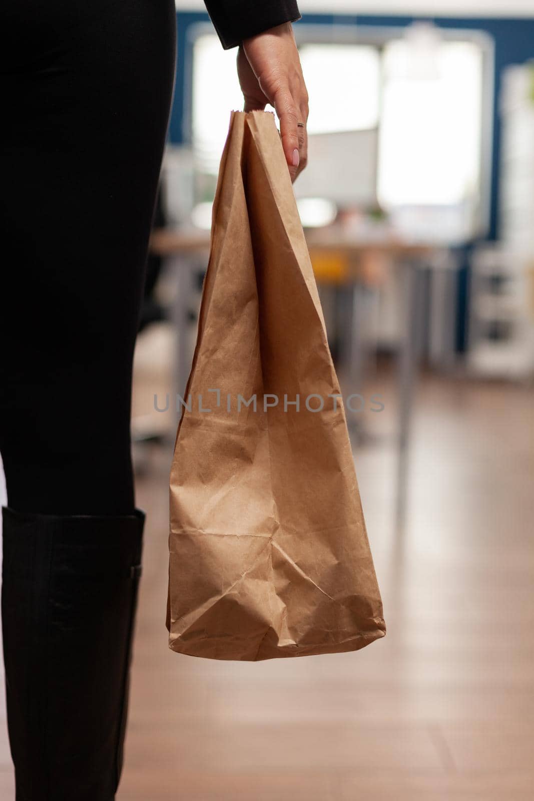Businesswoman holding delivery takeaway food meal order paper bag during takeout lunchtime putting at desk in startup company office. Entrepreneur woman having lunch service while working at strategy