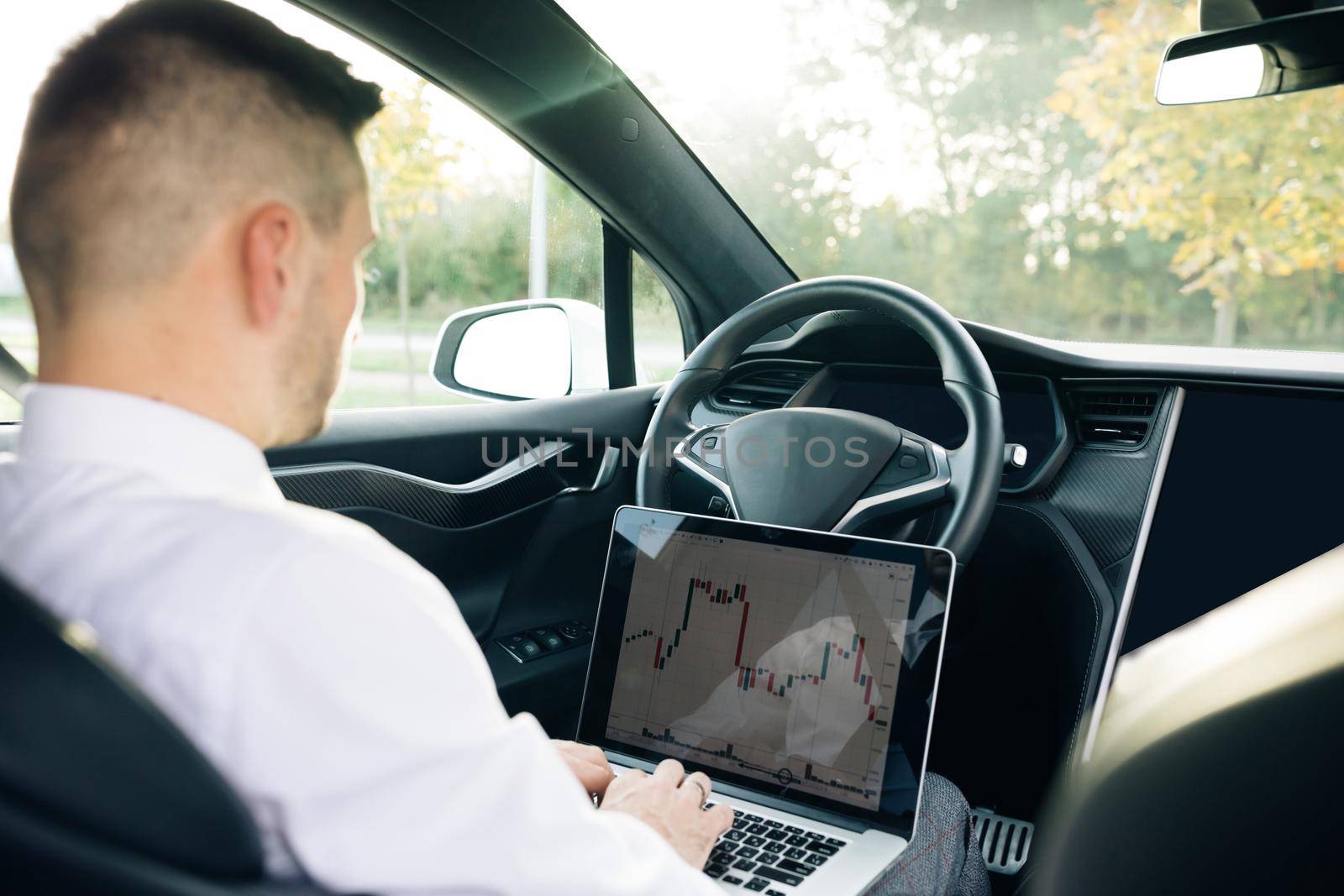 Successful businessman in formal outfit opening personal laptop while sitting in modern car. Bearded man using wireless computer in car. Stock market, trading online.