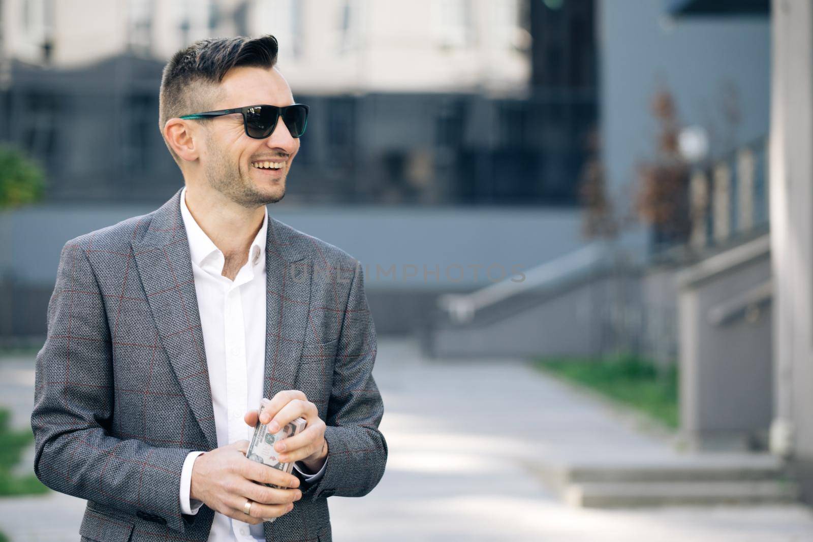 Amazed happy excited businessman with money - U.S. currency dollars banknotes. Man shows money and celebrating success, victory while looking to camera. Outdoors.