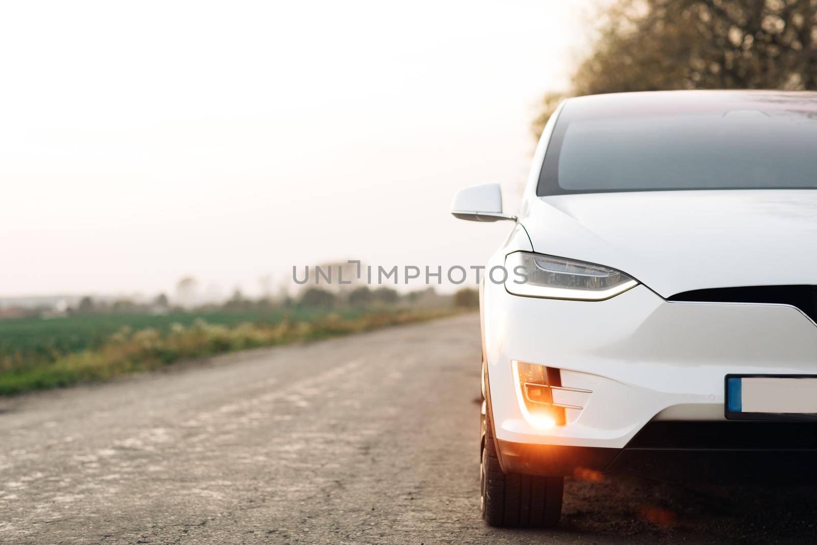 Electric Car on Country Road. Luxury modern vehicle along trees and fields. Electric Car on Gravel road with trees at sunset