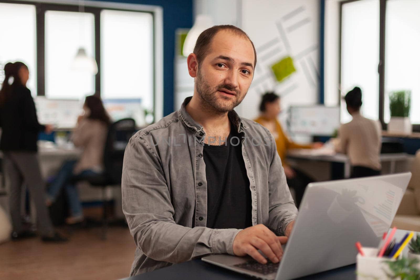 Business man sitting on desk looking at camera analysing financial statistics by DCStudio