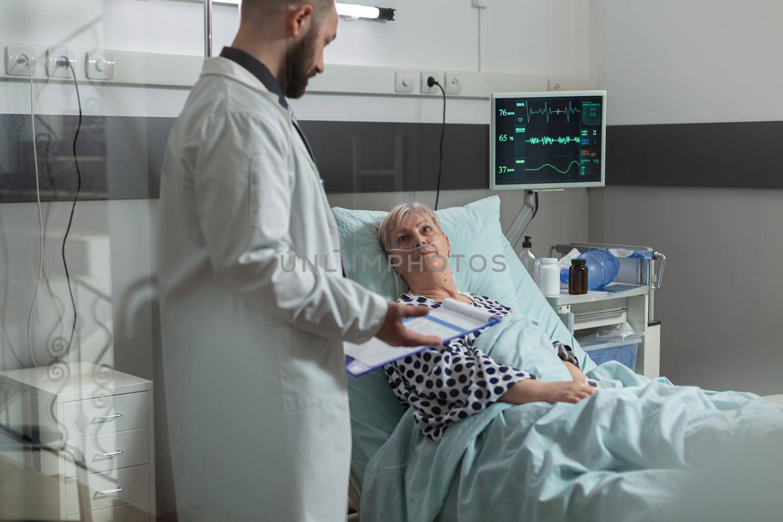 Sick senior woman lying in hospital bed listening doctor by DCStudio