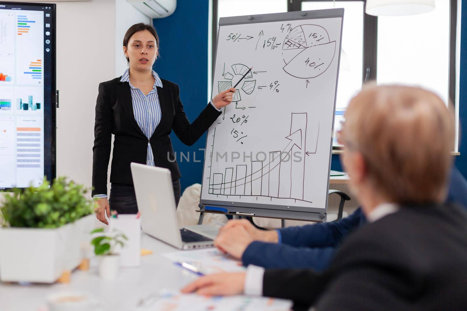 Leader making sales report for top company managers drawing charts on white board. Serious speaker boss executive, business trainer explaining development strategy to motivated mixed race employees.