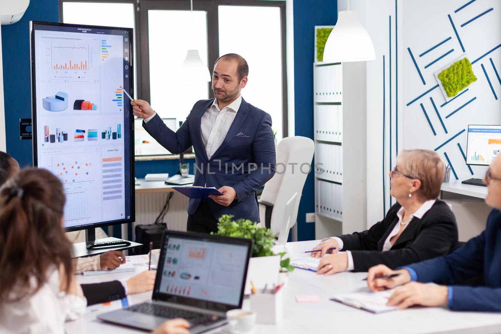 Business partner presenting company strategy to diverse team brainstorming in new startup office, analysing financial graphs Multiethnical businesspeople working in professional board financial office conference meeting.