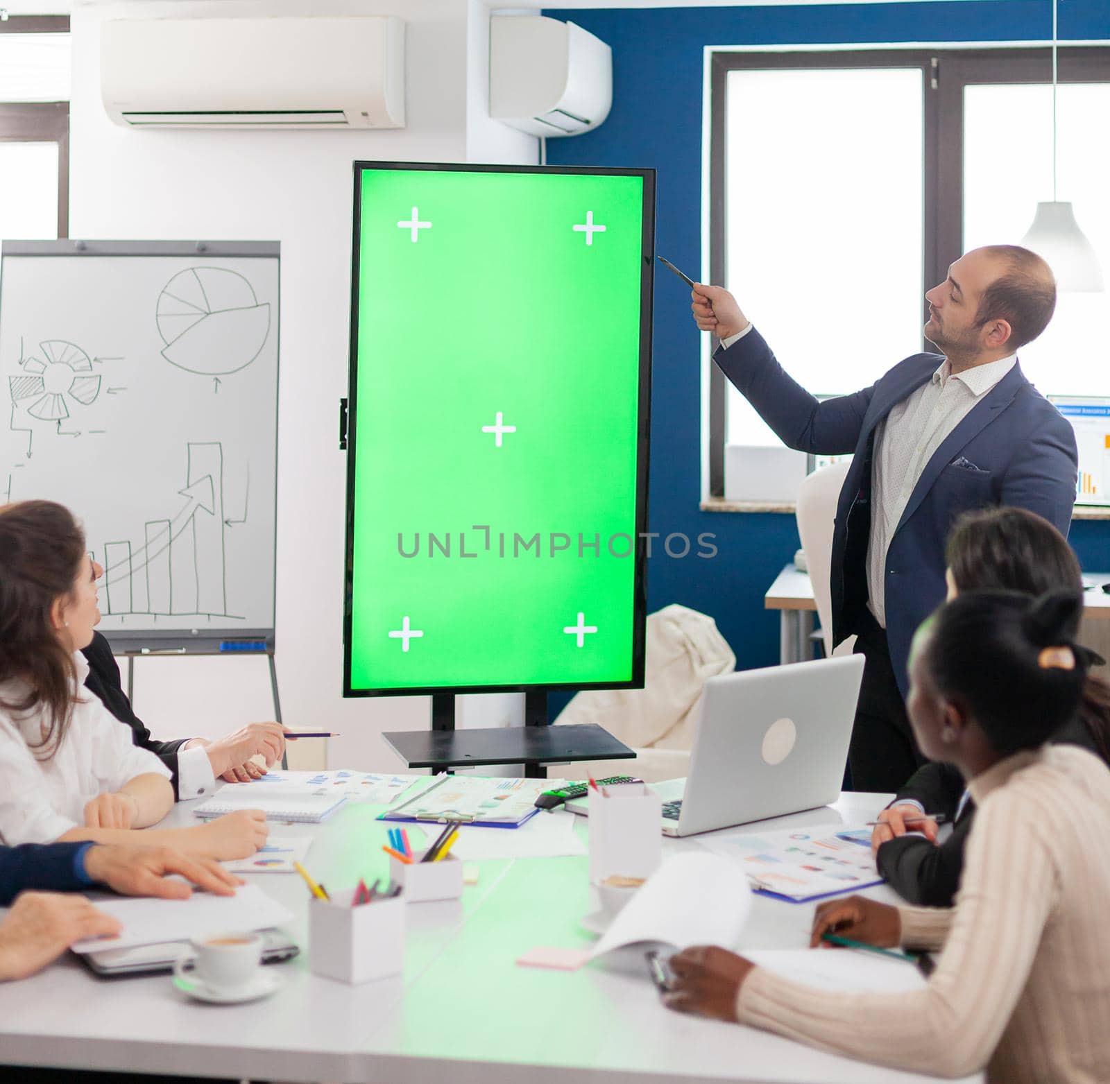 Leader of company presenting financial plan using mockup display in front of diverse team brainstorming. Manager explainig project strategy on green screen monitor with chroma key desktop in boardroom