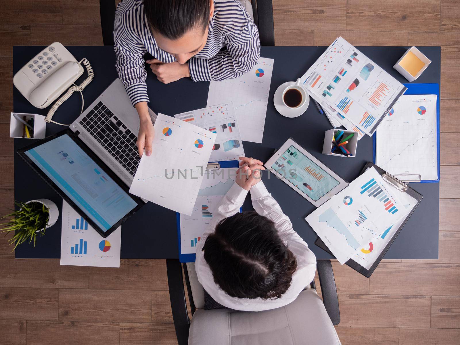 Top view of office workers meeting analyzing financial charts holding clipboard. Manager and employer discussing marketing strategy during briefing. Pointing at graphs. Business teamwork startup meeting