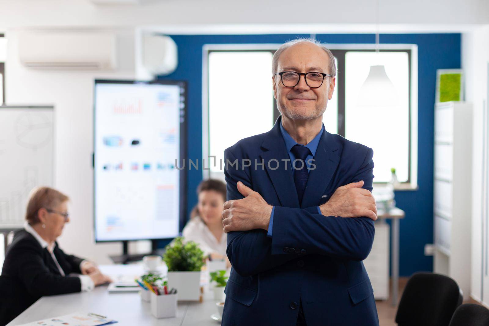 Portrait of succesful senior entrrepeneur in conference room smiling at camera with arms crossed. Manager working in professional start up financial business, modern company workplace ready for meeting.