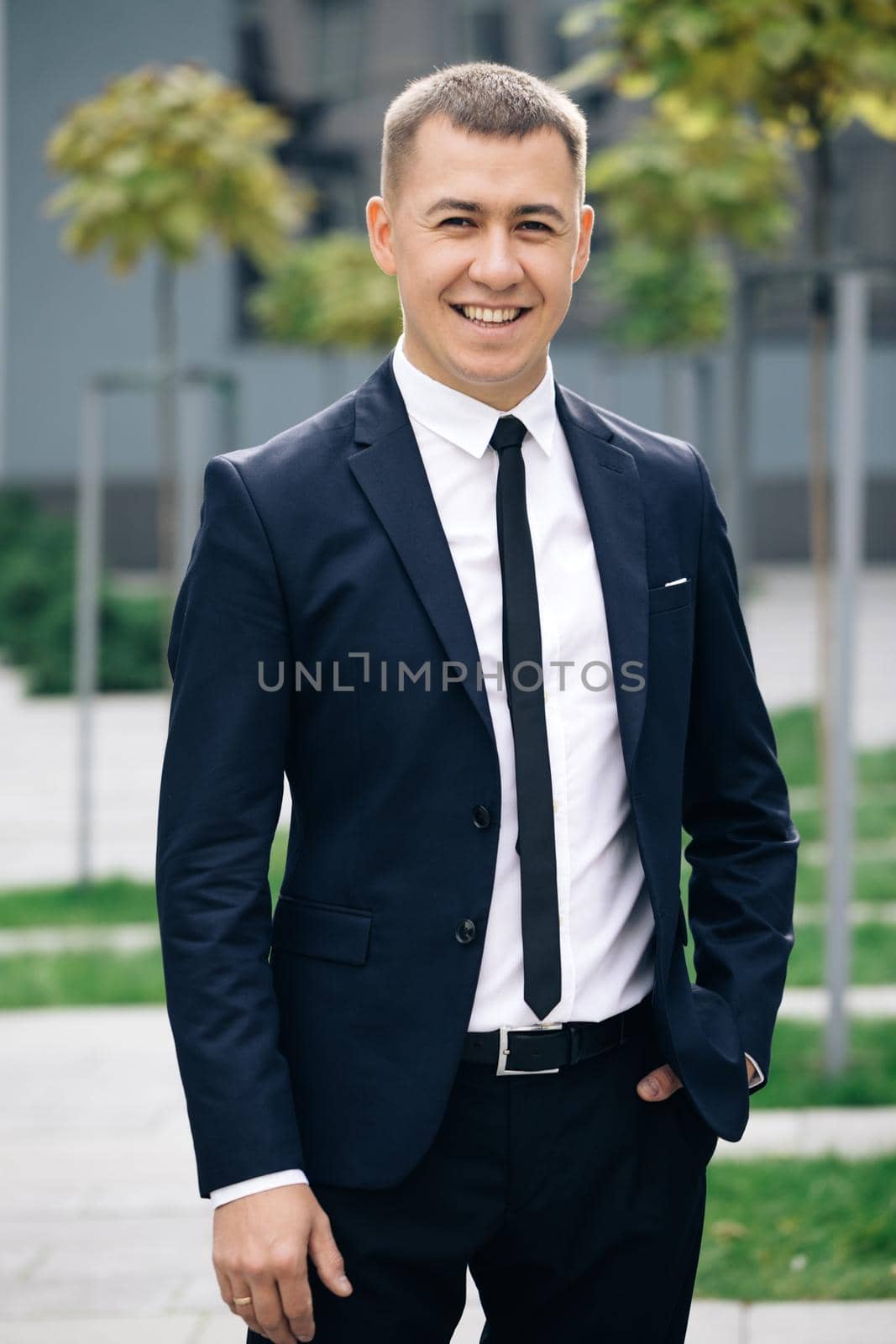 Happy cheerful man looking straight with smile. Successful career attractive manager handsome confident. Portrait of handsome man in tie smiling cheerfully to camera at street near business center by uflypro