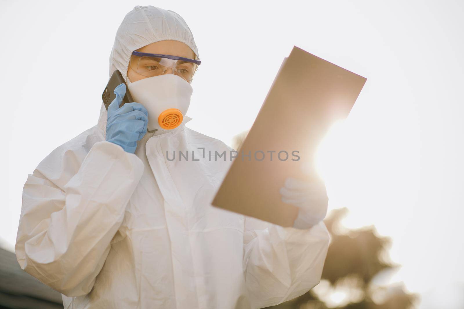 Doctor epidemiologist fighting with coronavirus COVID-19. Female Doctor Wearing a Facemask and Suit Stands Outside in the Sunset. Nurse wears a protective suit and mask during the COVID19 outbreak.