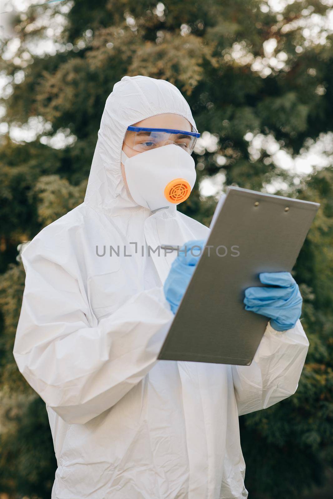 Doctor epidemiologist fighting with coronavirus COVID-19. Coronavirus Protection Pandemic Threat Covid 19. Woman in a Protective Insulating Suit and Mask notes the Data in a Notebook. by uflypro