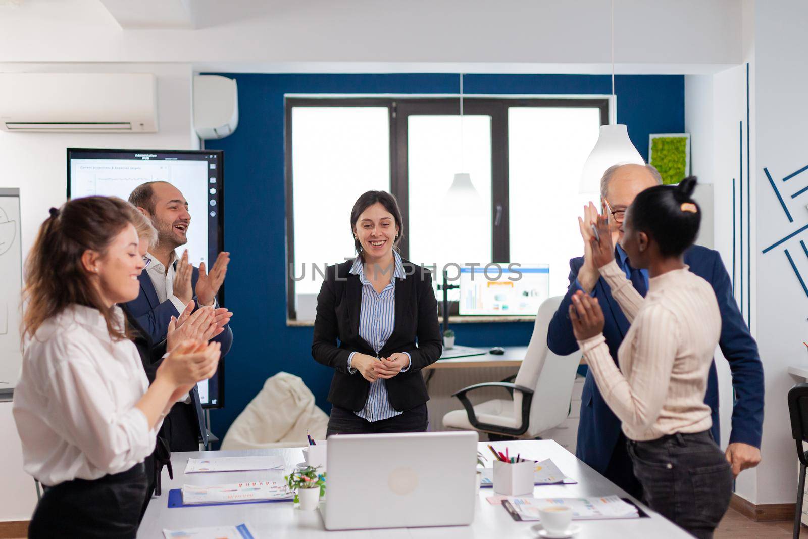 Happy overjoyed financial startup team standing clapping a in conference briefing. Multiethnical partners coworkers celebrate successful teamwork result at company briefing