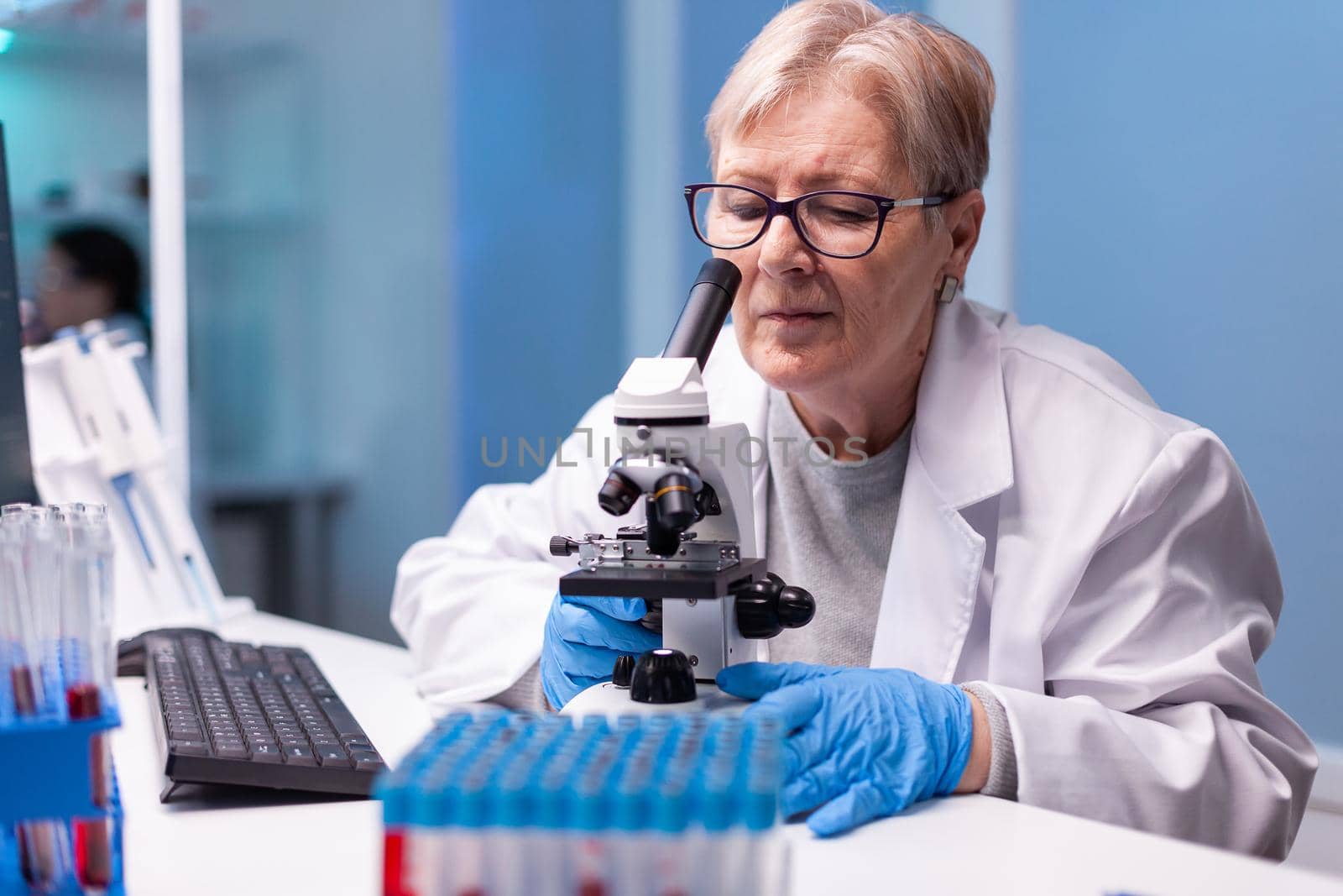 Senior doctor in white coat looking into microscope in laboratory discovery. Modern lab with research equipment for virus study and vaccine science development
