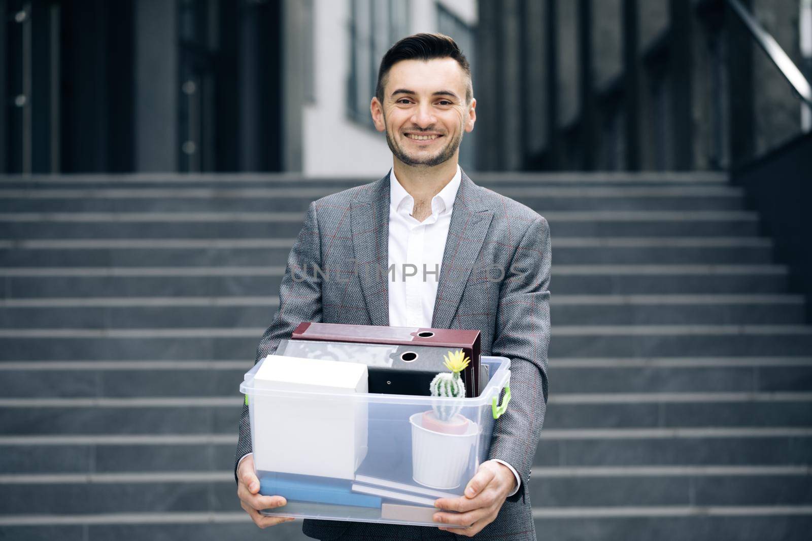 Happy businessman returns to work after vacation. New employee on first day at work carrying box with stuff to his new workplace. Concept of work career and success by uflypro