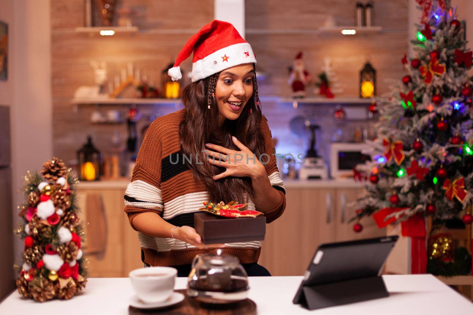 Happy woman using video call conference app on tablet giving virtual christmas present in festive home. Caucasian young person showing winter gifts with friends preparing for reunion