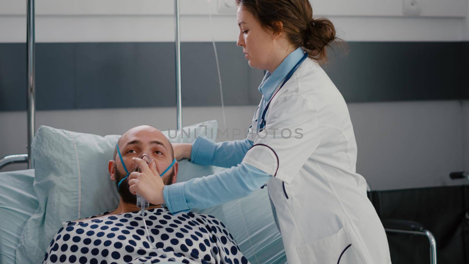 Close up of sick man patient resting in bed while doctor putting oxygen mask monitoring respiratory illness in hospital ward during healthcare emergency. Physician analyzing heartbeat pluse