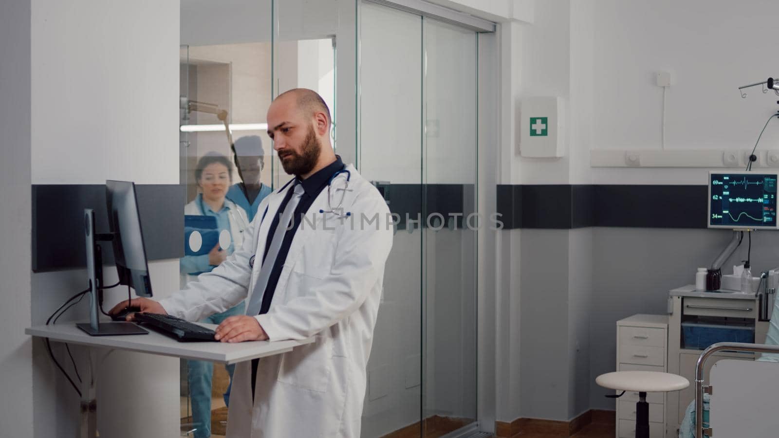 Doctor practitioner in uniform analyzing disease diagnosis typing illness treatment on computer working in hospital ward. Medical team discussing with sick patient while resting in bed after surgery