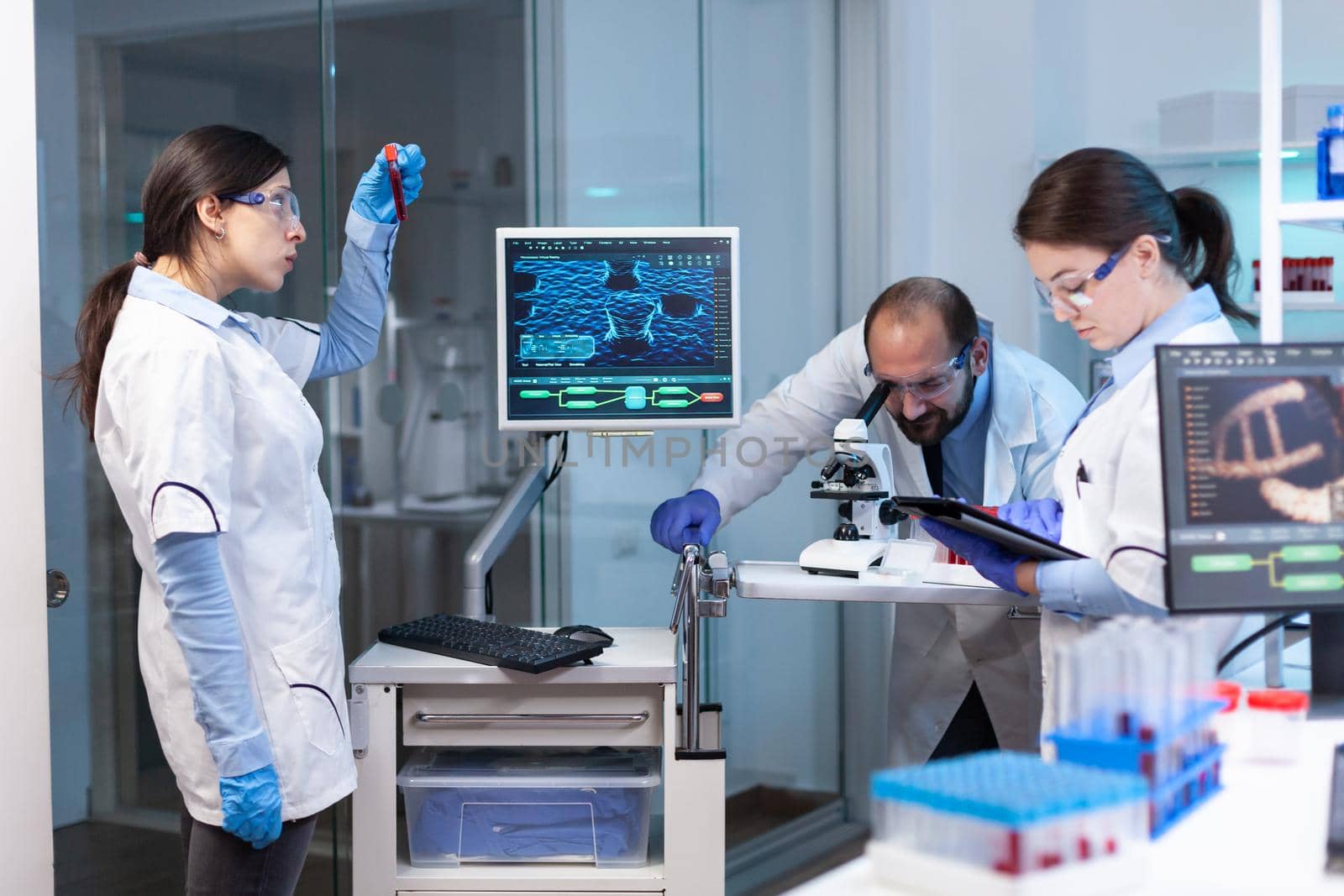 Research scientists working on monitor with medical equipment analyzing blood, genetic material samples. Doctors specialists discussing treatment against covid19 virus using high technology equipment