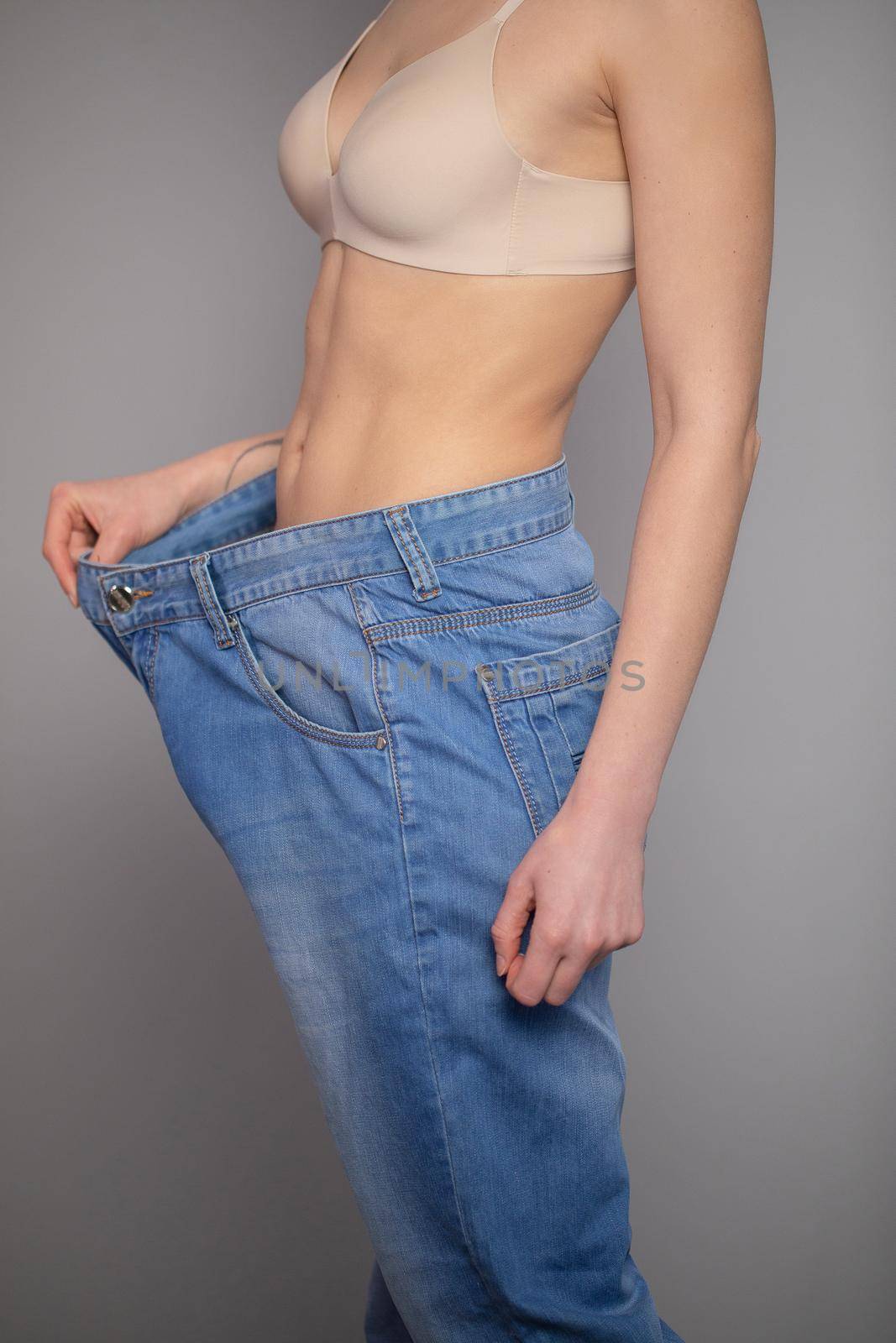 Woman Shows her Weight Loss and Wearing Her Old Jeans. Slim Girl in Big Jeans Showing How She Was Losing Weight When She Started Eating Healthy Food. by uflypro