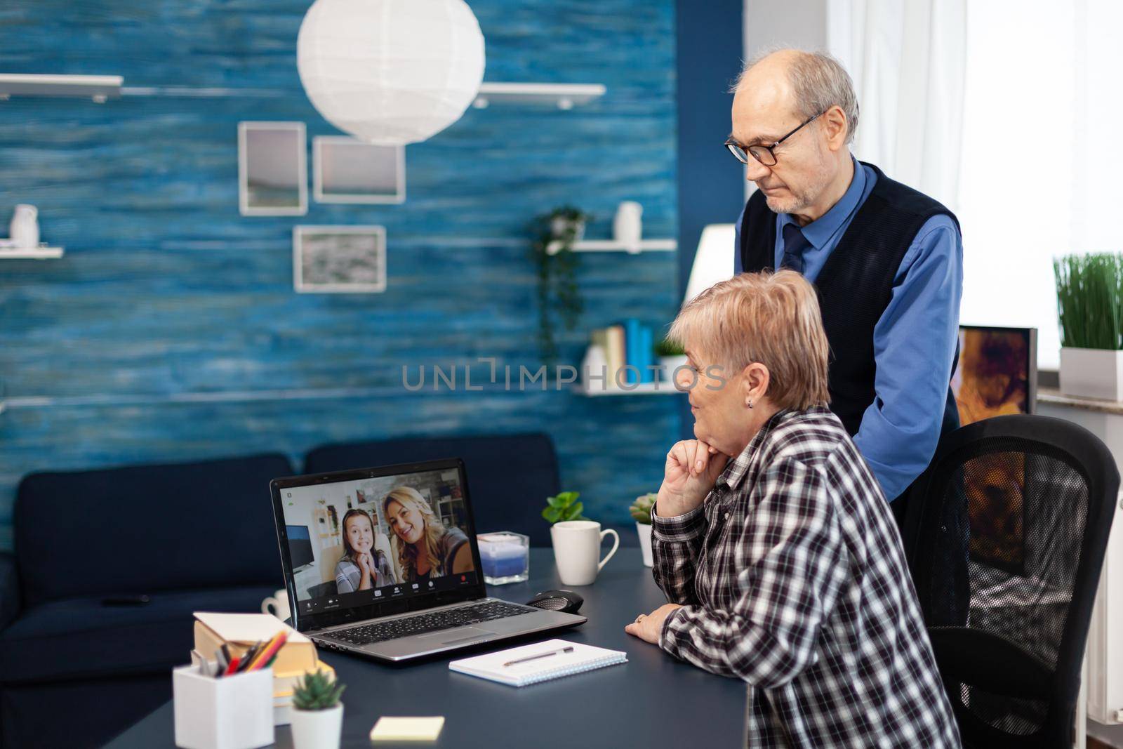 Senior man and woman talking with niece on video call. Happy grandparents communicating with family via online web internet video conference using modern internet technology while sitting in the living room