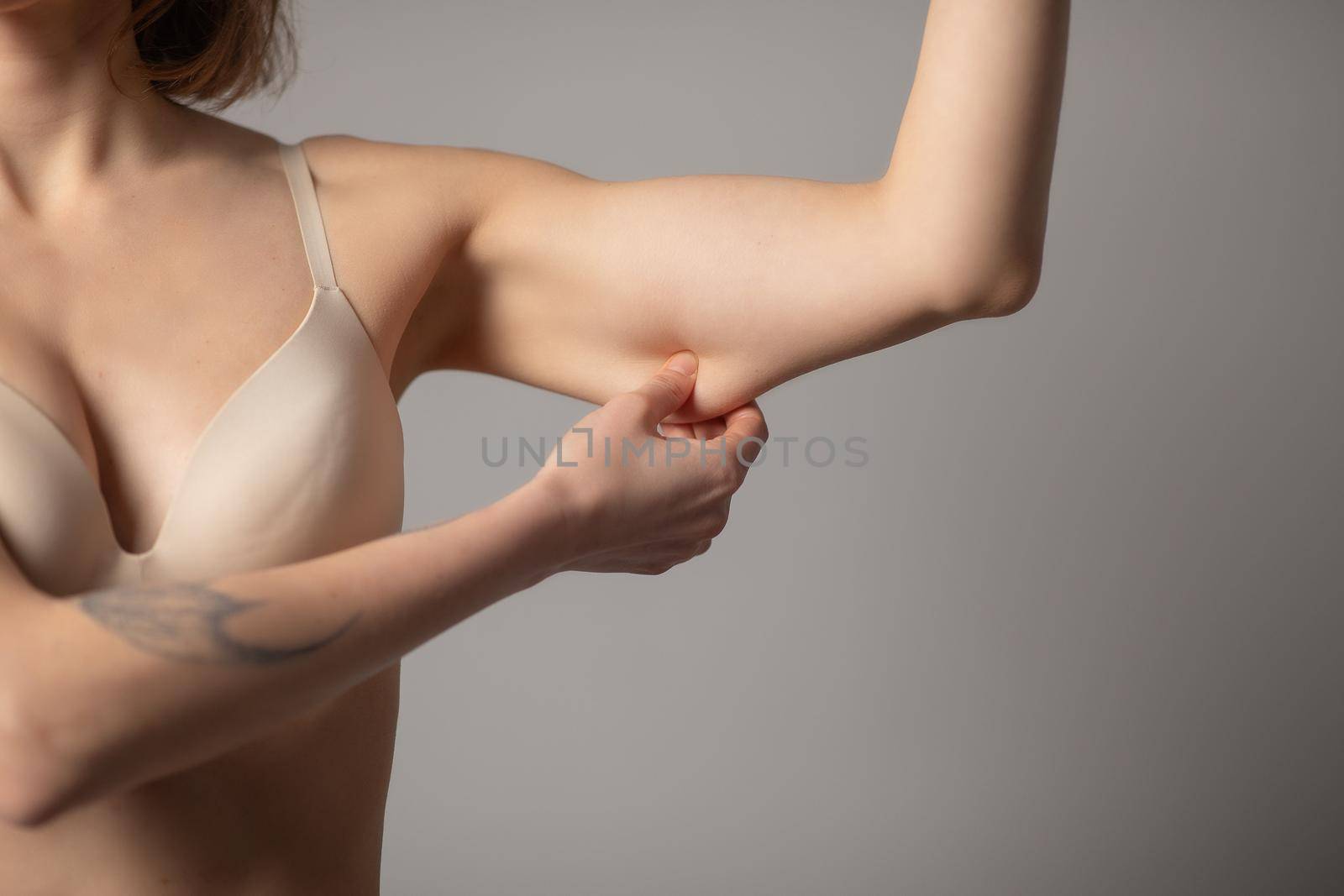 Chubby Woman Pinching Upper Arm Fat Isolated on Grey Background. Close up of Caucasian Female Hand Checking Flabby Skin. Body Control, Time to go on Diet and Weight Loss Concept