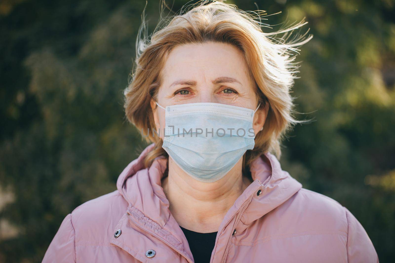 Woman in Medical Mask. Breathes deeply and looking at camera on green background outdoor. Health care and medical concept.