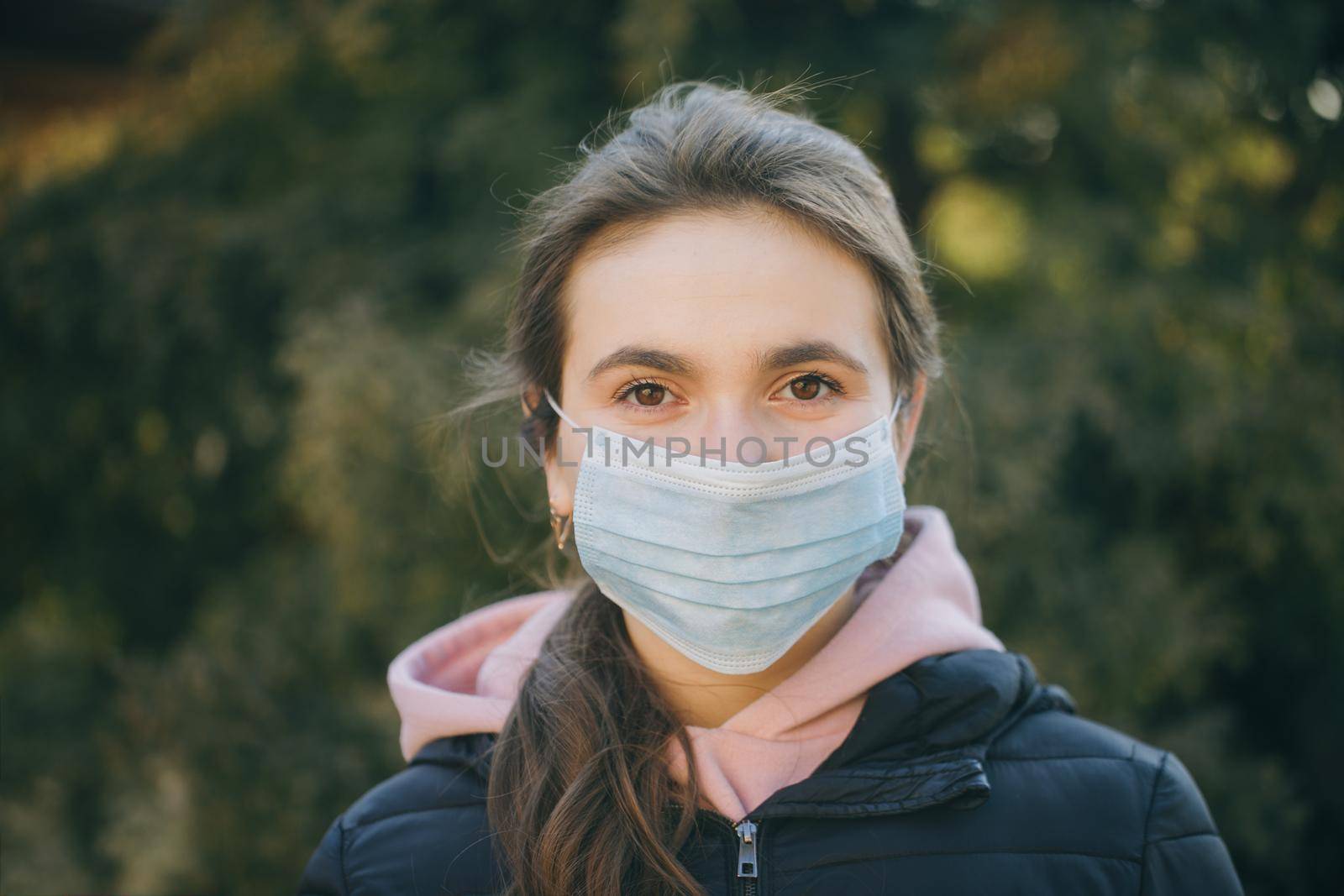 Sick girl wearing protection during pandemic. Pretty young Caucasian girl taking on medical mask outdoor. Girl Wearing Medical Mask During Coronavirus COVID-19 Epidemic