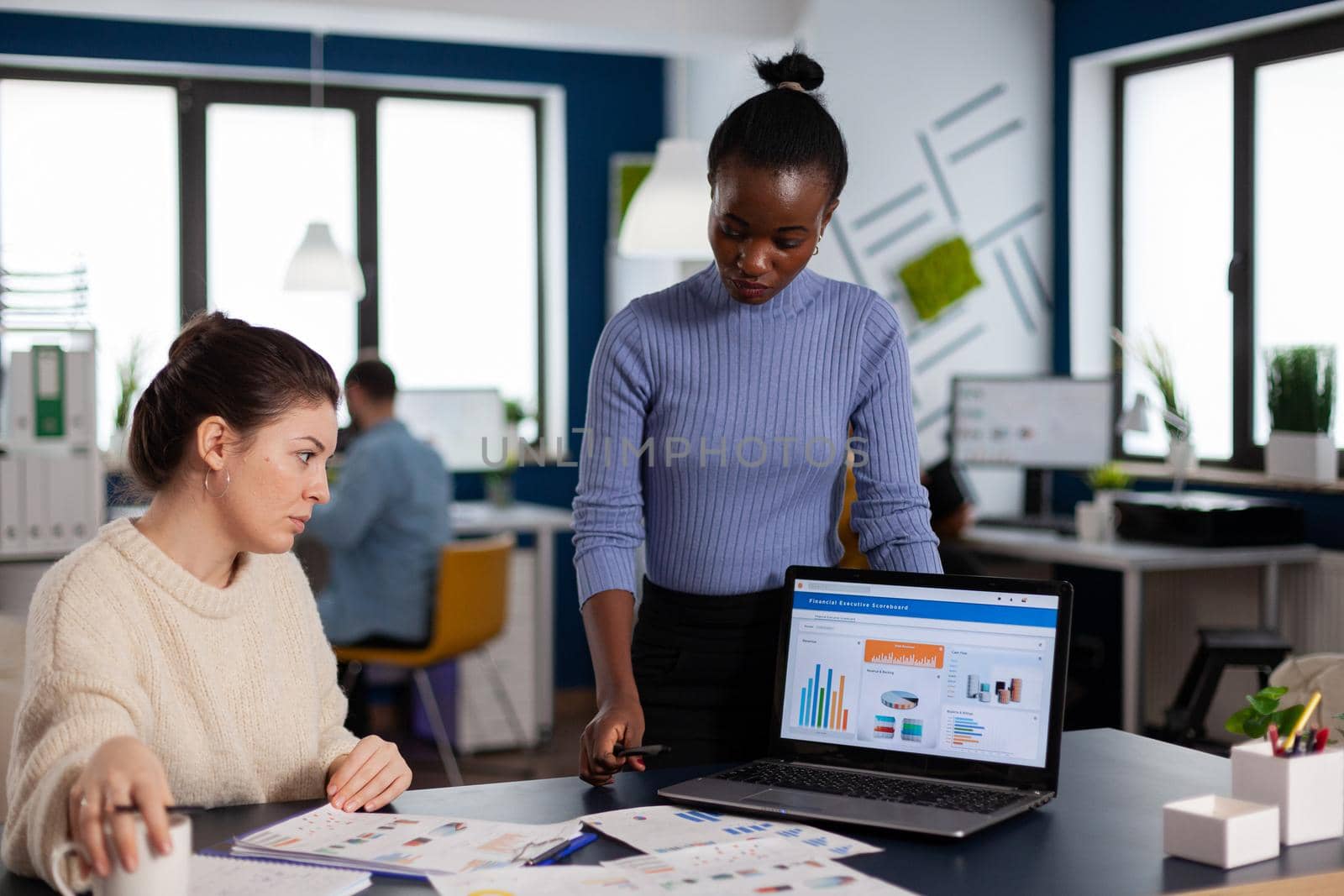 Diverse businesswomen discussing new project for company evolution, black woman checking tasks on new contract. Multiethnic employees gathered in co-working space.