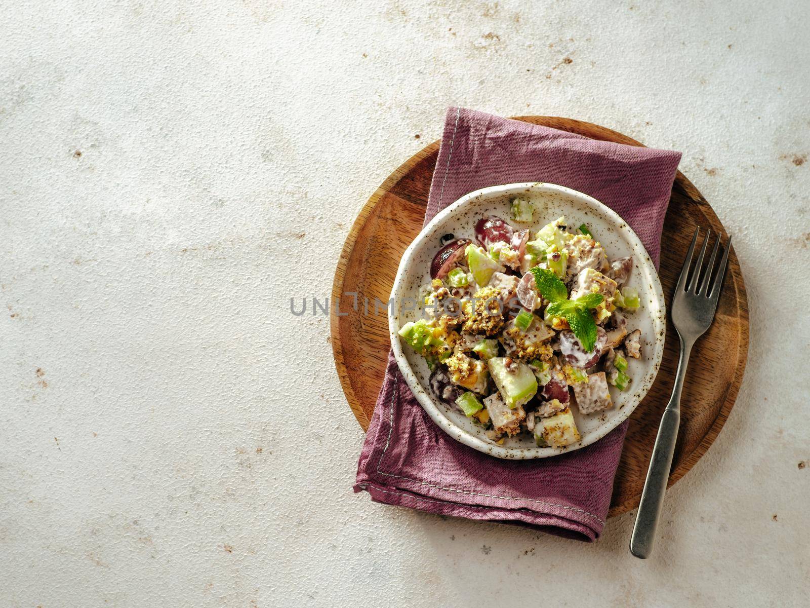 Waldorf salad with copy space. American fruit and nut salad with apples, celery, grapes, chicken meat, dressed mayonnaise. Craft plate with ready-to-eat waldorf salad on light background. Top view