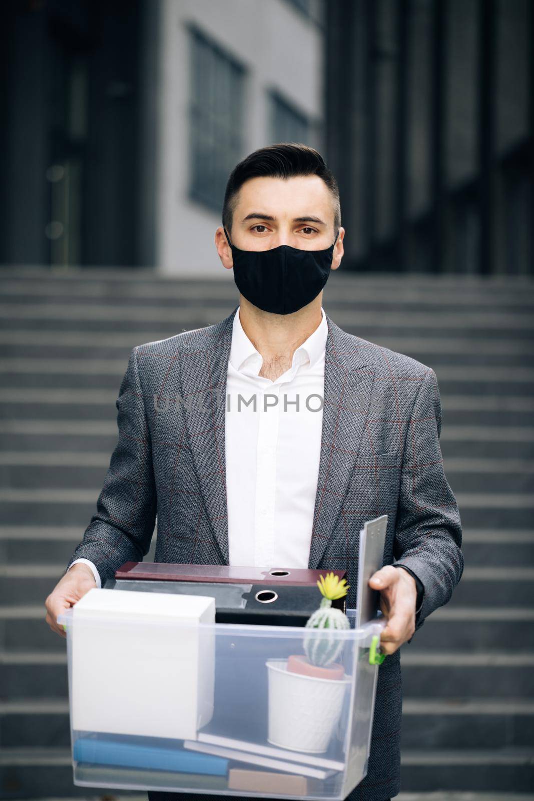 Young businessman in medical mask carries box with personal belongings leaving the office. Lack of jobs. Financial crisis. Unemployment.