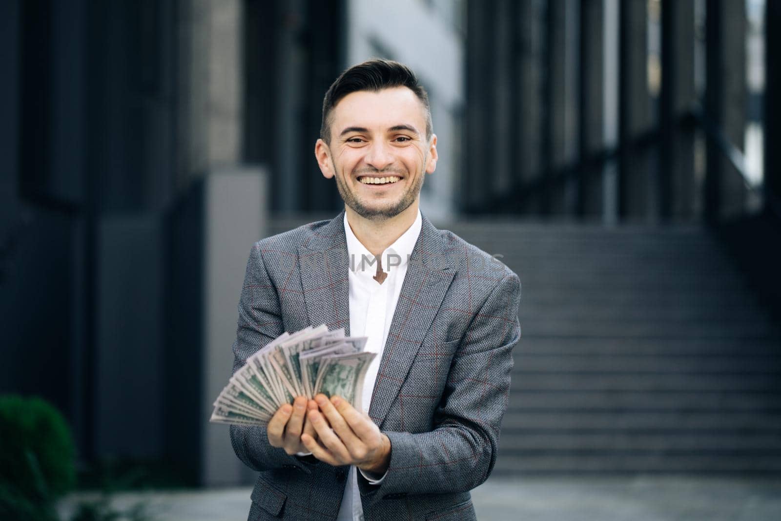 Amazed happy excited businessman with money - U.S. currency dollars banknotes. Man shows money and celebrating success, victory while looking to camera. Outdoors.
