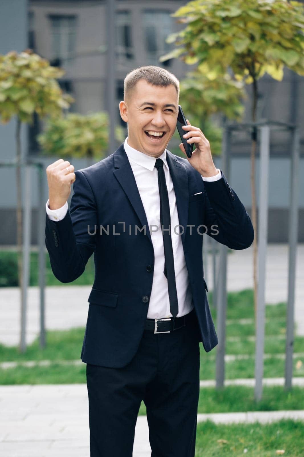 Happy person reading good news on mobile phone outdoors. Surprised man celebrating victory at remote workplace. Successful in suit boss company confident. Vertical screen orientation. by uflypro