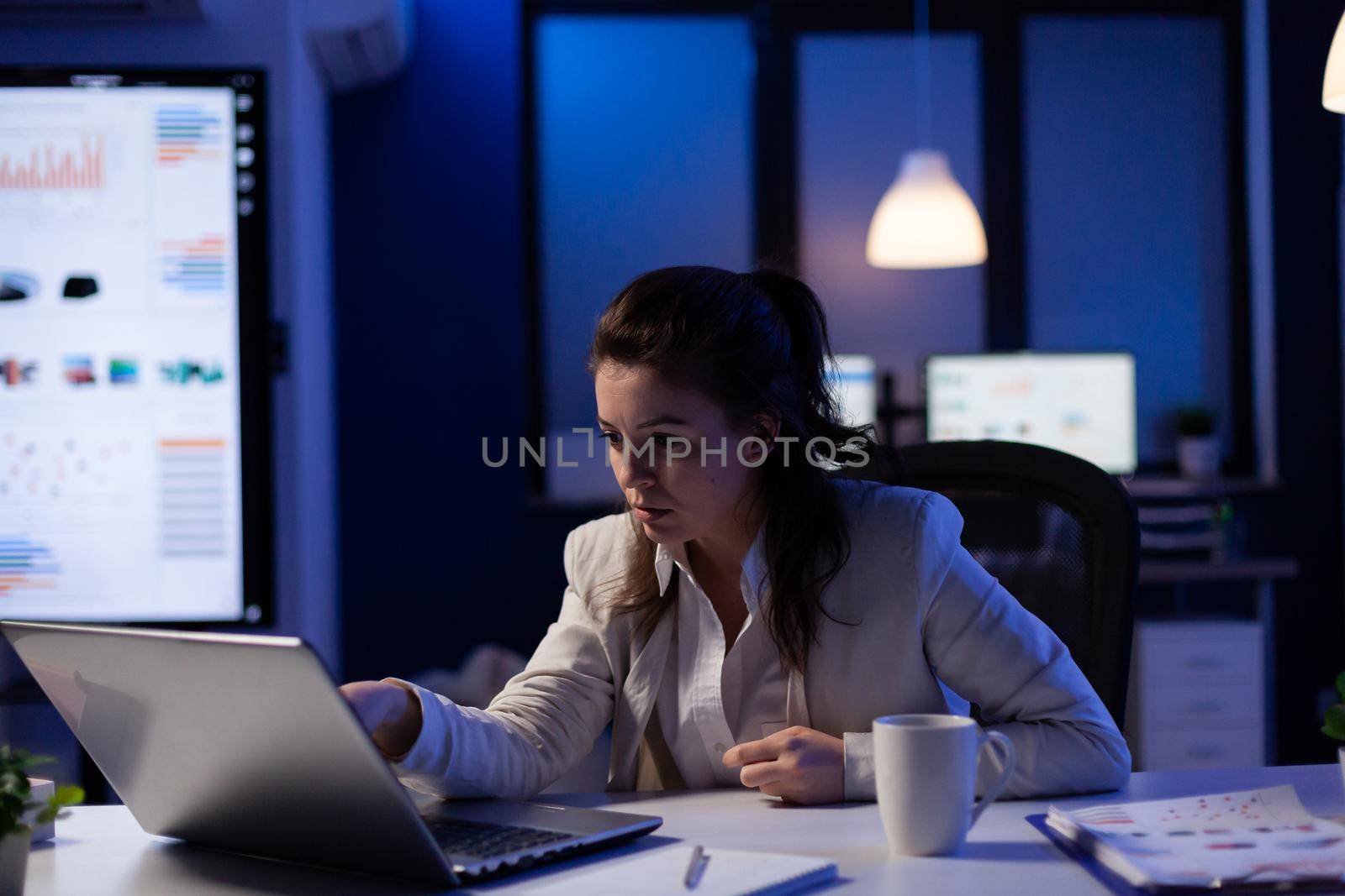 Stressed businesswoman checking profit resultes standing in business office late at night. Focused entrepreneur using technology network wireless for developing new marketing system