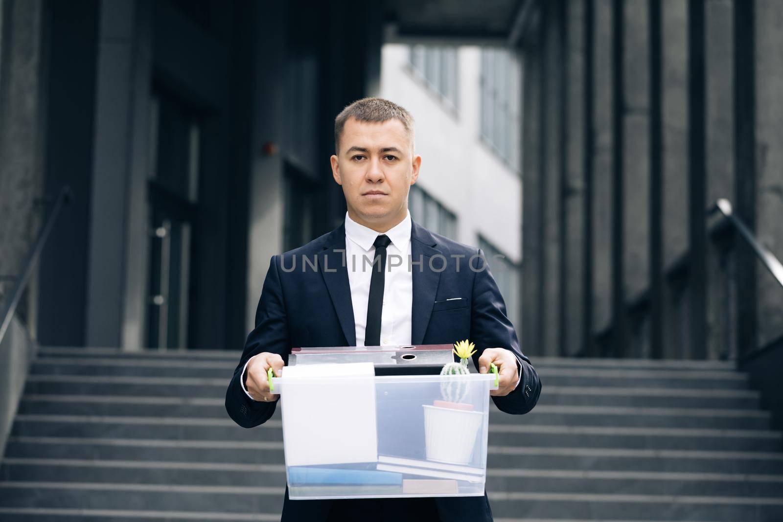 Portrait sad male office worker in depression with box of personal stuff. Businessman lost job. Fired man outdoors. Depressed jobless person. Unemployment concept. Left without money by uflypro