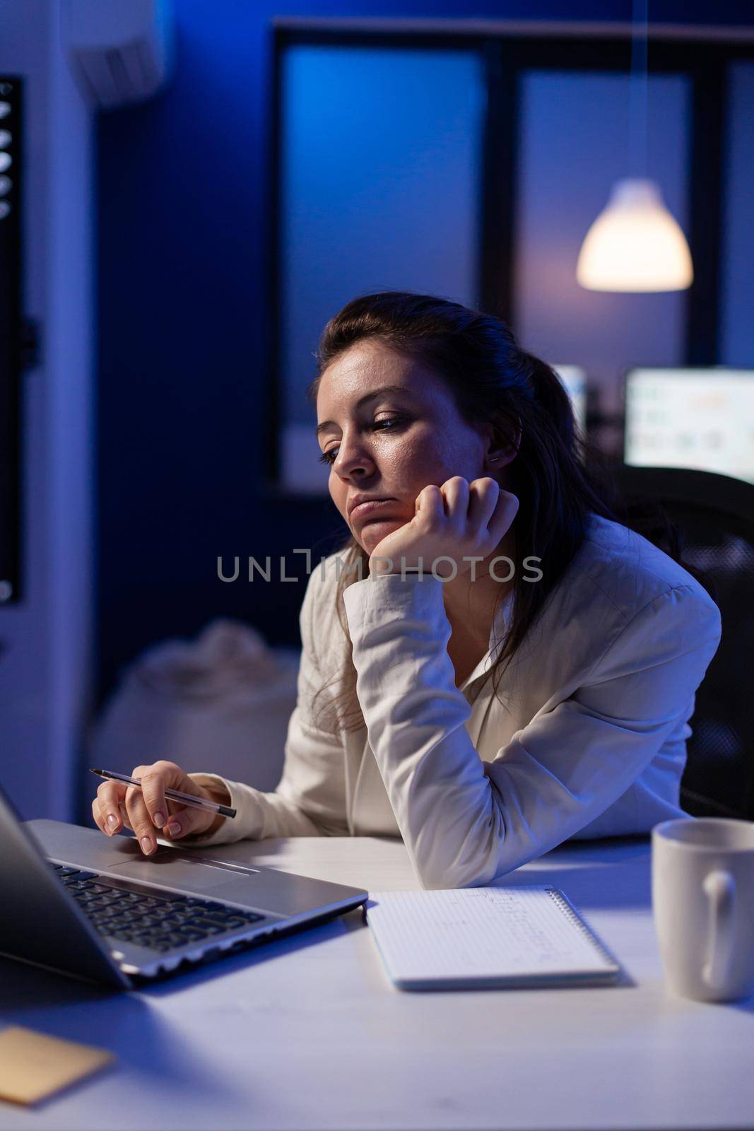 Tired remote woman talking nap on chair working on laptop, analysing financial statistics in company office. Busy woman using modern technology network wireless late at night