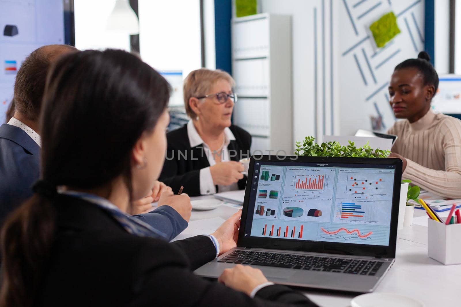Young woman analysing charts on laptop in business meeting room by DCStudio