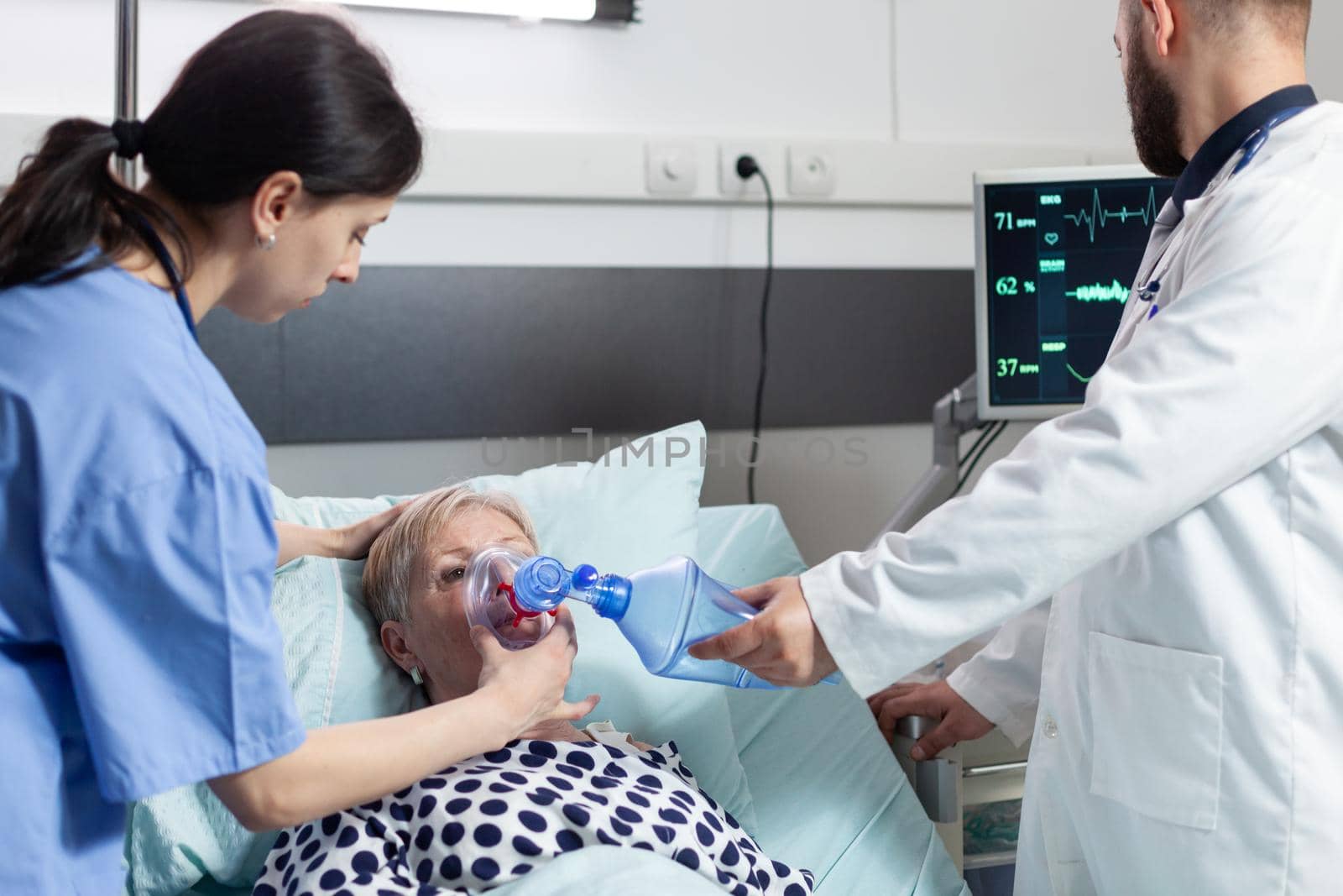 Medical team helping senior woman patient laying in hospital bed by DCStudio