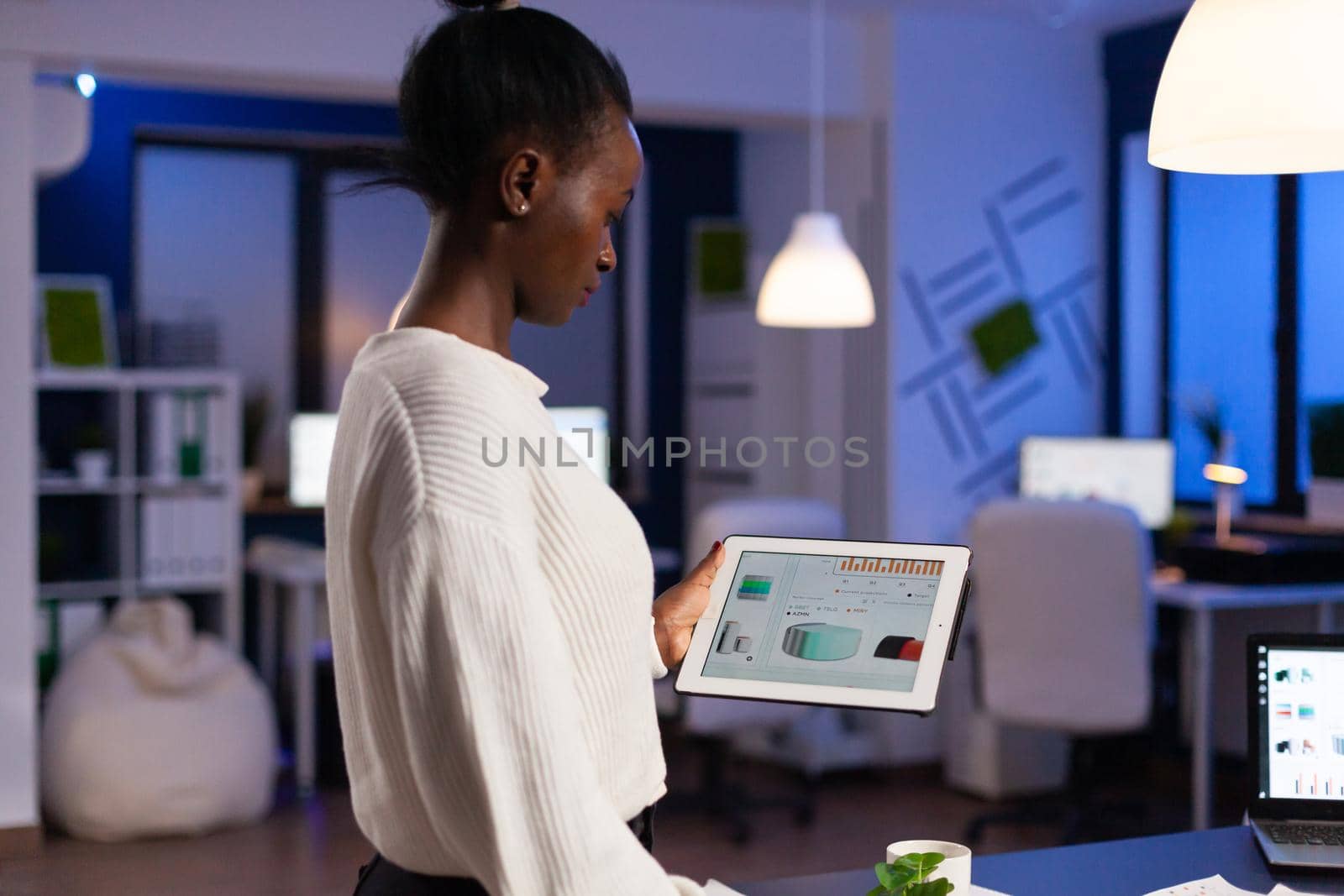 Black woman working on deadline analysing charts on tablet pc by DCStudio