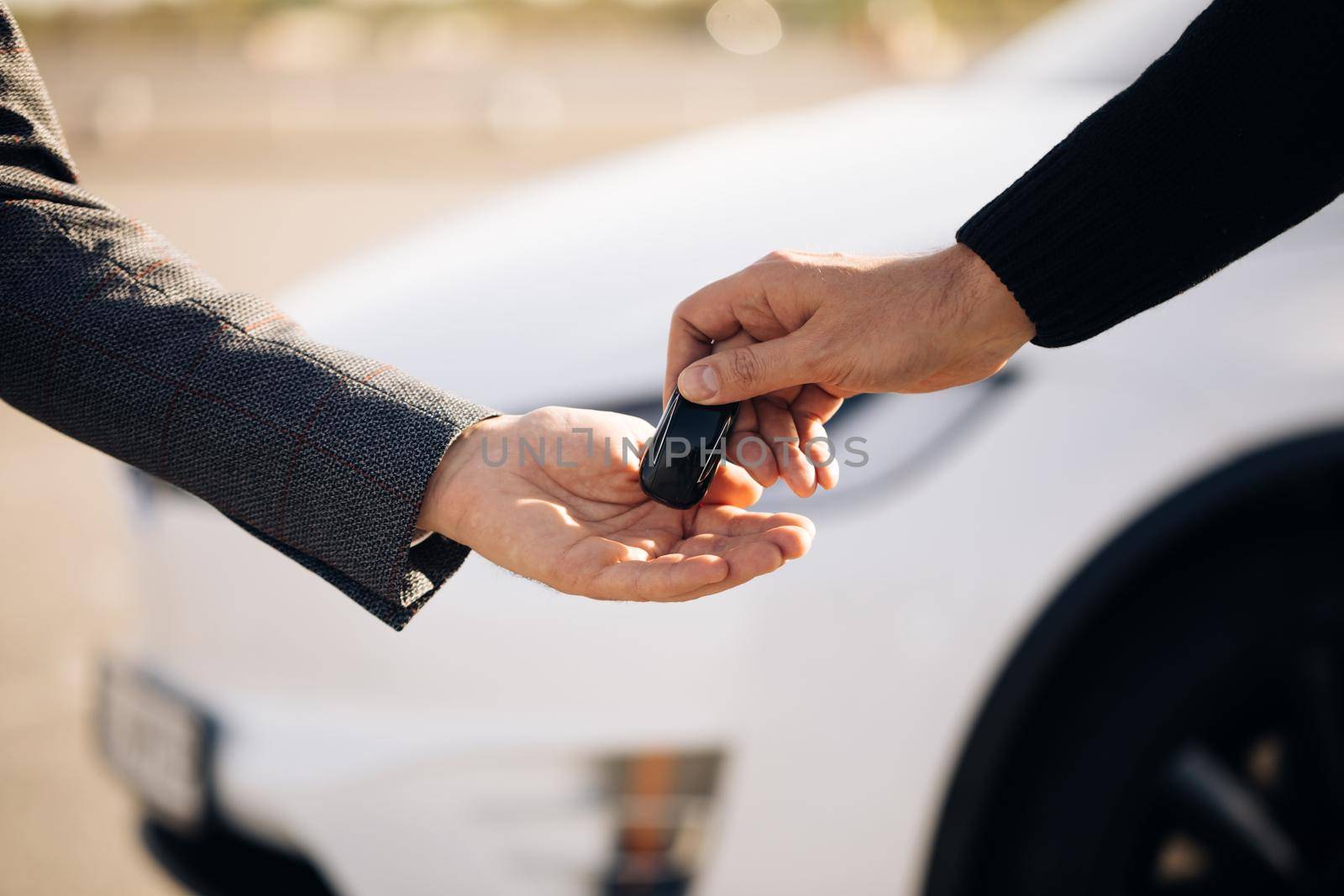 Male hand gives a car keys to male hand in the car dealership close up. Unrecognized auto seller and a man who bought a vehicle. Dealer giving key to new owner in auto show or salon.