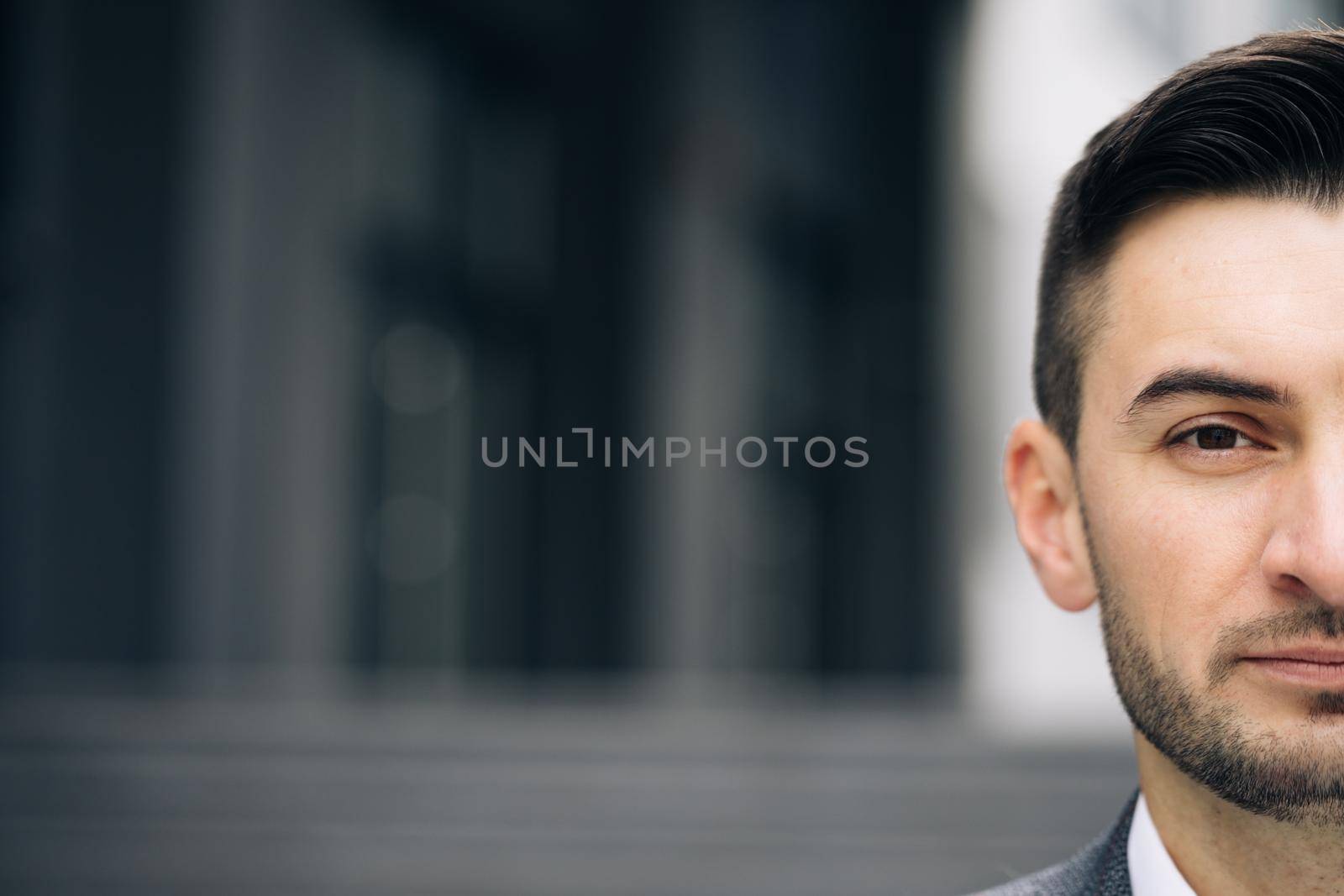 Close up of male half face at street with architecture. Portrait of caucasian handsome man looking at camera. Businessman concept. Outdoor.