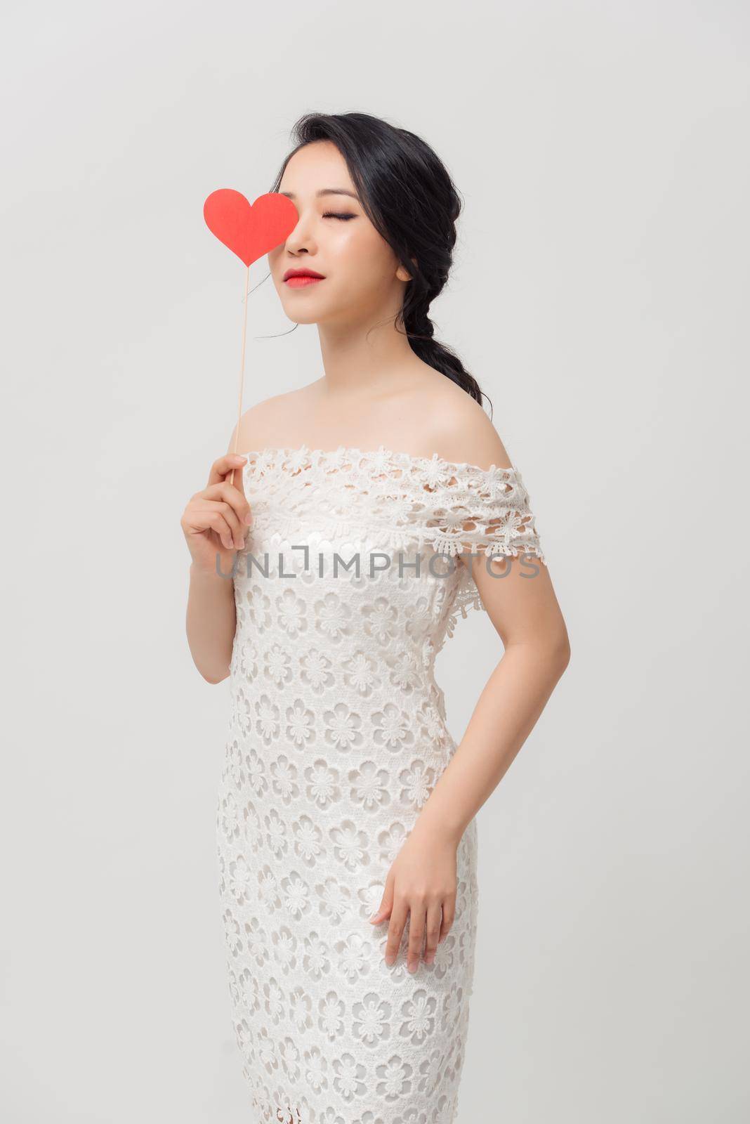 Elegant Asian woman holding a parper heart and standing isolated over white background.