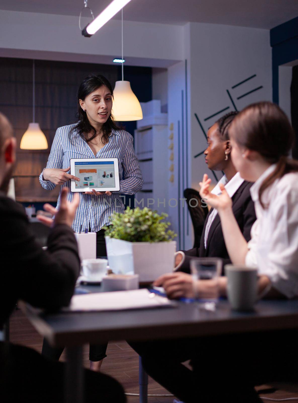 Business leader in meating room late at night discussing with her team by DCStudio