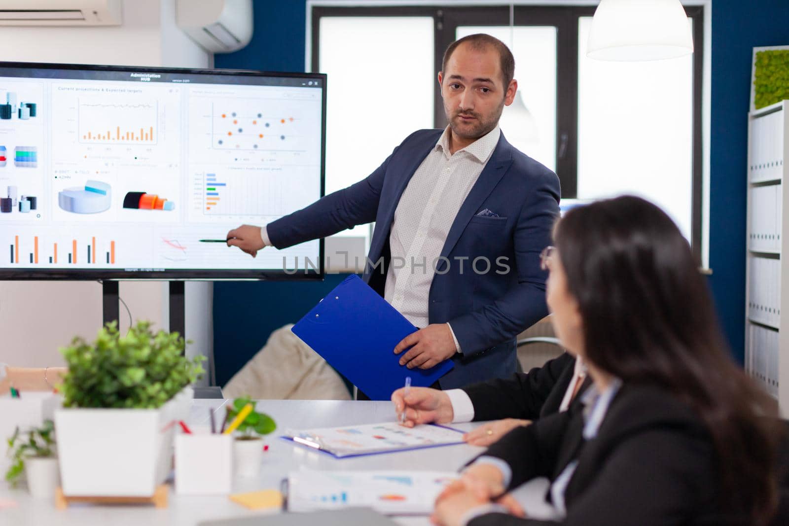 Successful team leader briefing pointing explaining project in conference room brainstorming. Corporate staff discussing new business application with colleagues looking at screen