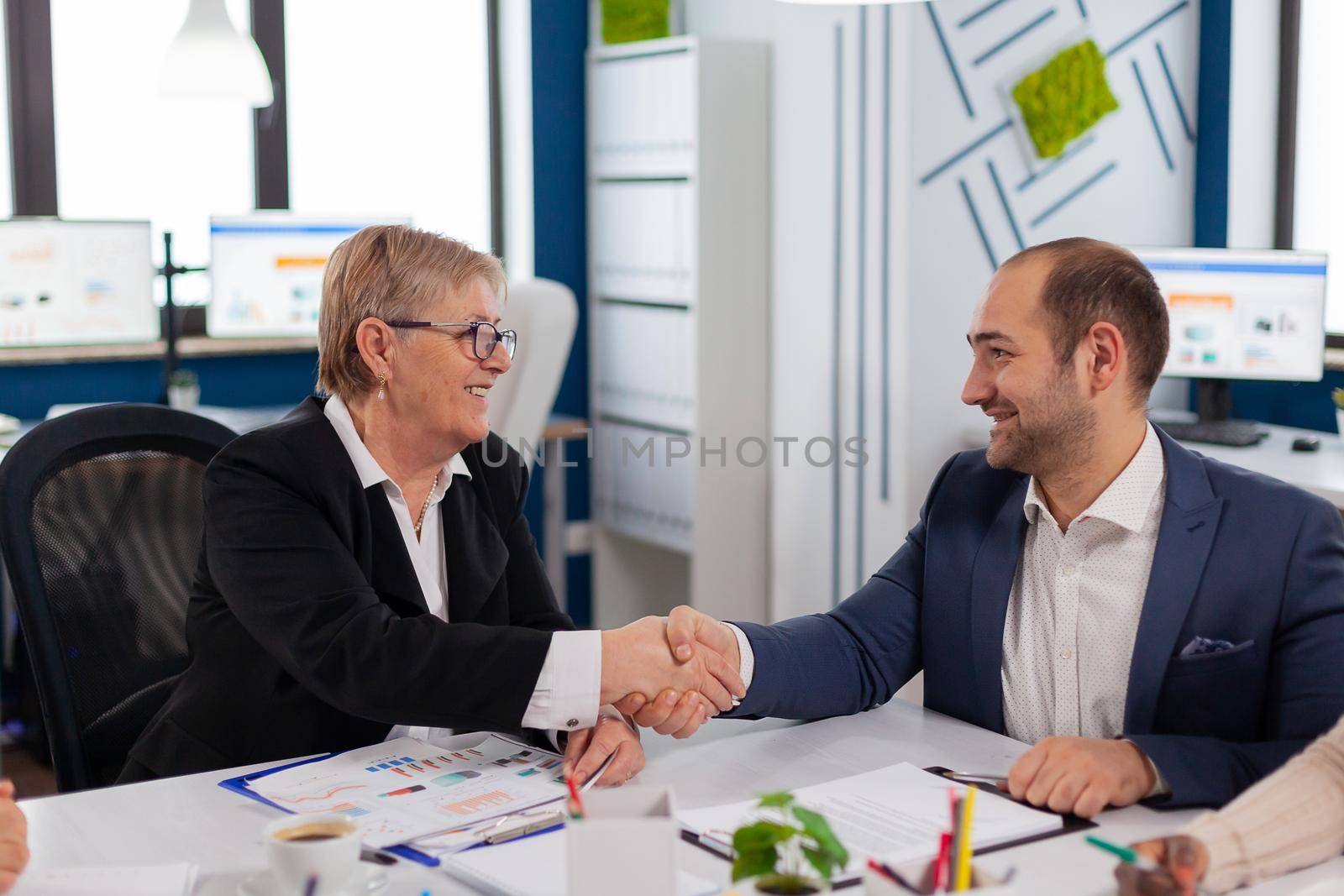 Young businessman reading documents, sign its and consultant greeting international client with handshake after planning partnership deal. Executive director meeting shareholders in start up office