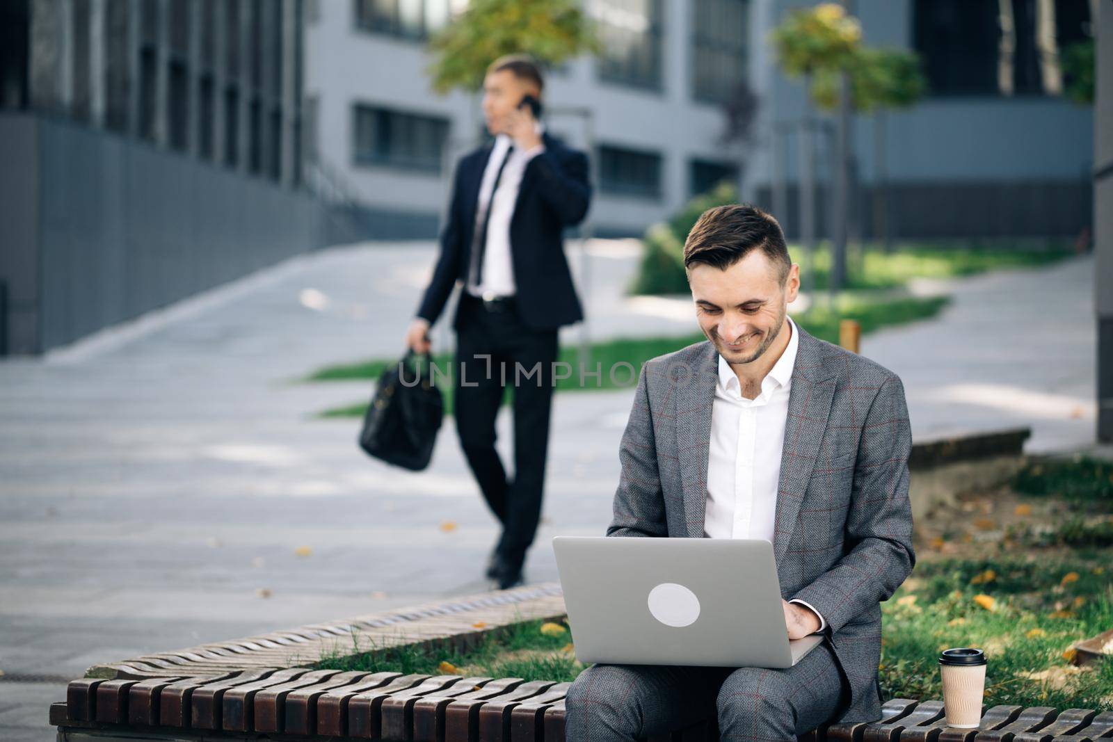Caucasian businessman in suit and tie communication while typing on laptop sitting outside. Distance working. Isolated man on a suit by uflypro