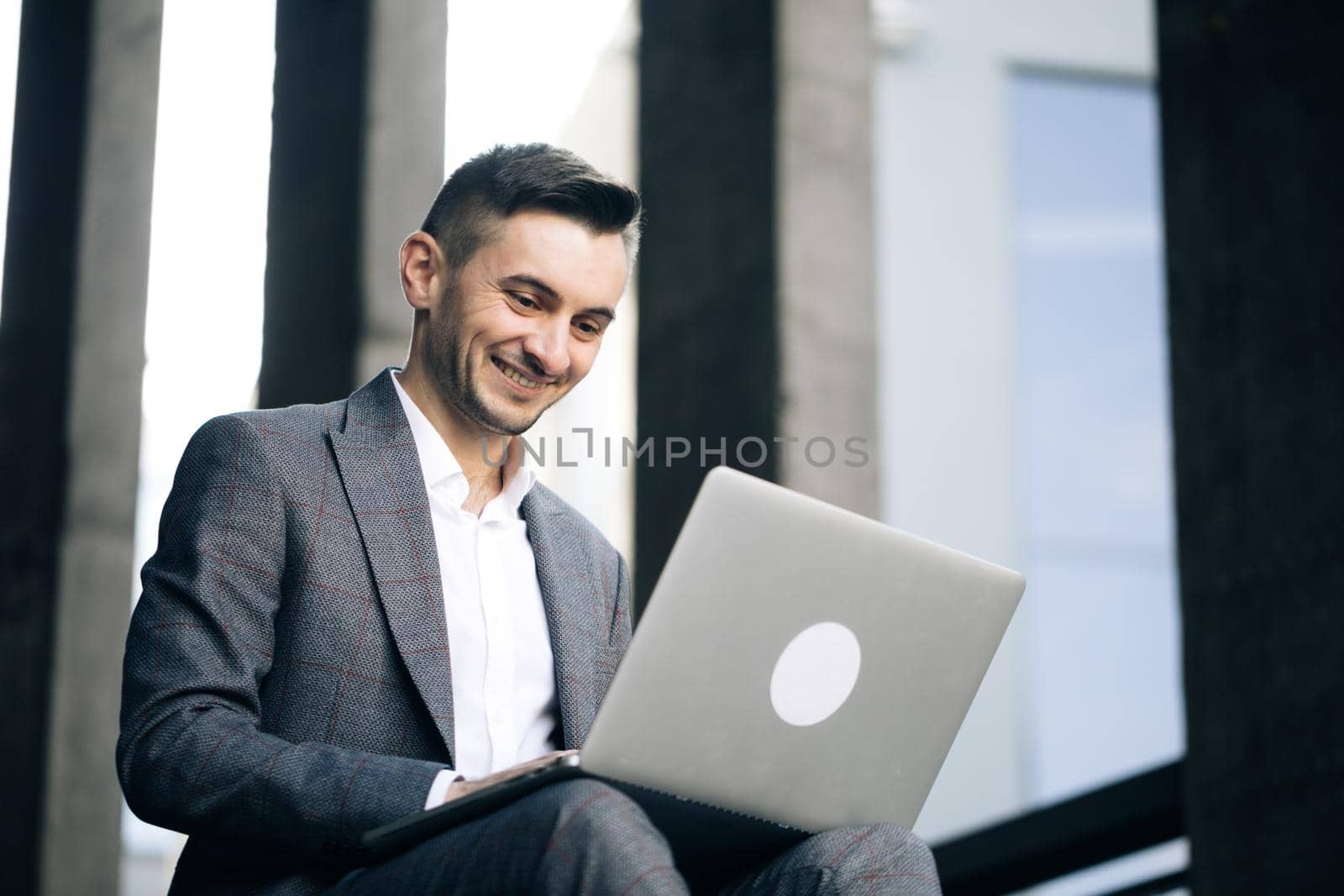 Working remotely and Self isolation. Bearded man working with laptop computer outside the office. Caucasian young man siting on steps outdoor and working on laptop computer.