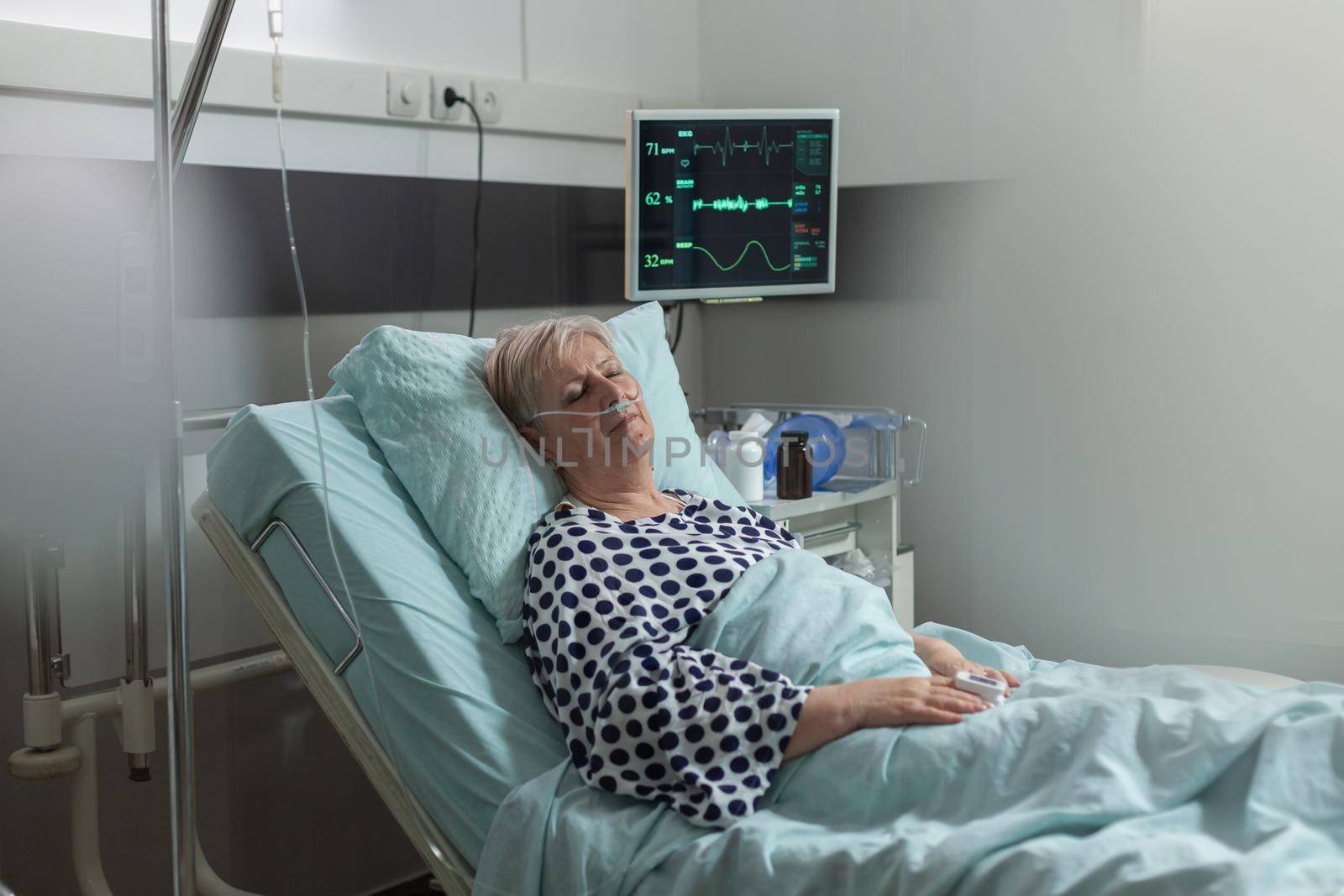 Senior woman patient in hospital room getting medicine through intravenous line by DCStudio