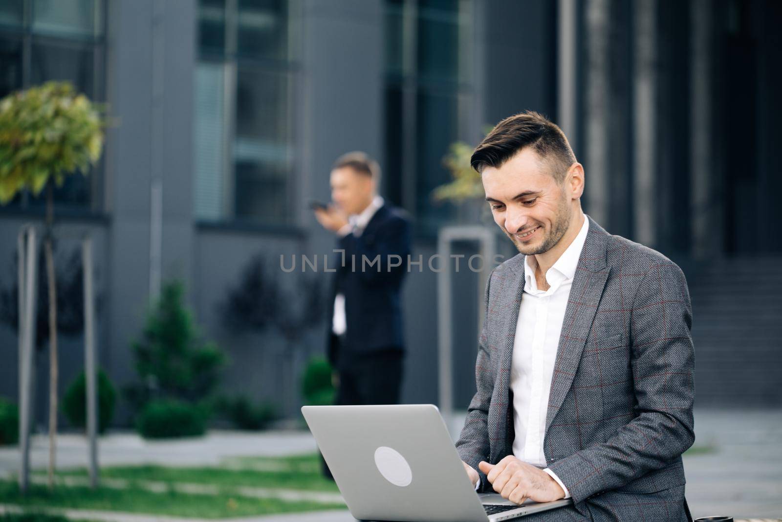 Distance working. Isolated man on a suit. Caucasian businessman in suit and tie communication while typing on laptop sitting outside.