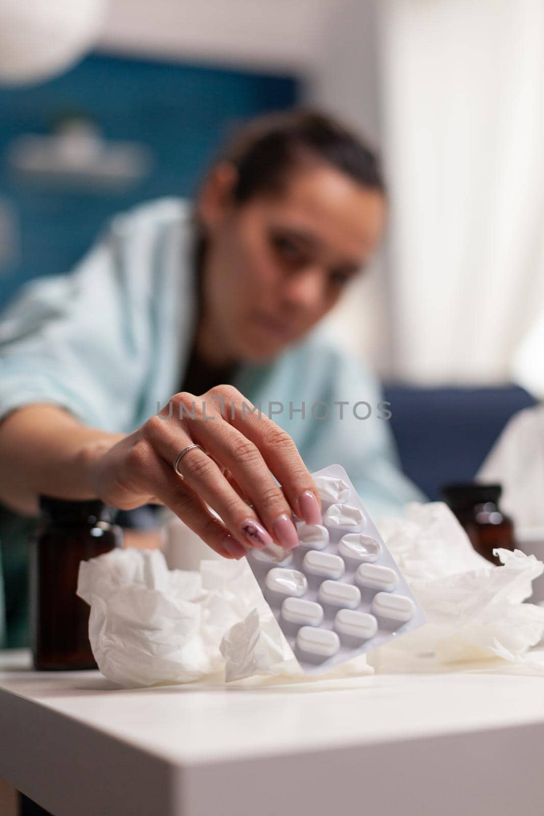 Young woman resting from virus symptoms at home while taking medical treatment medicine tablet drugs for illness. Caucasian adult having seasonal cold fever temperature on couch indoors